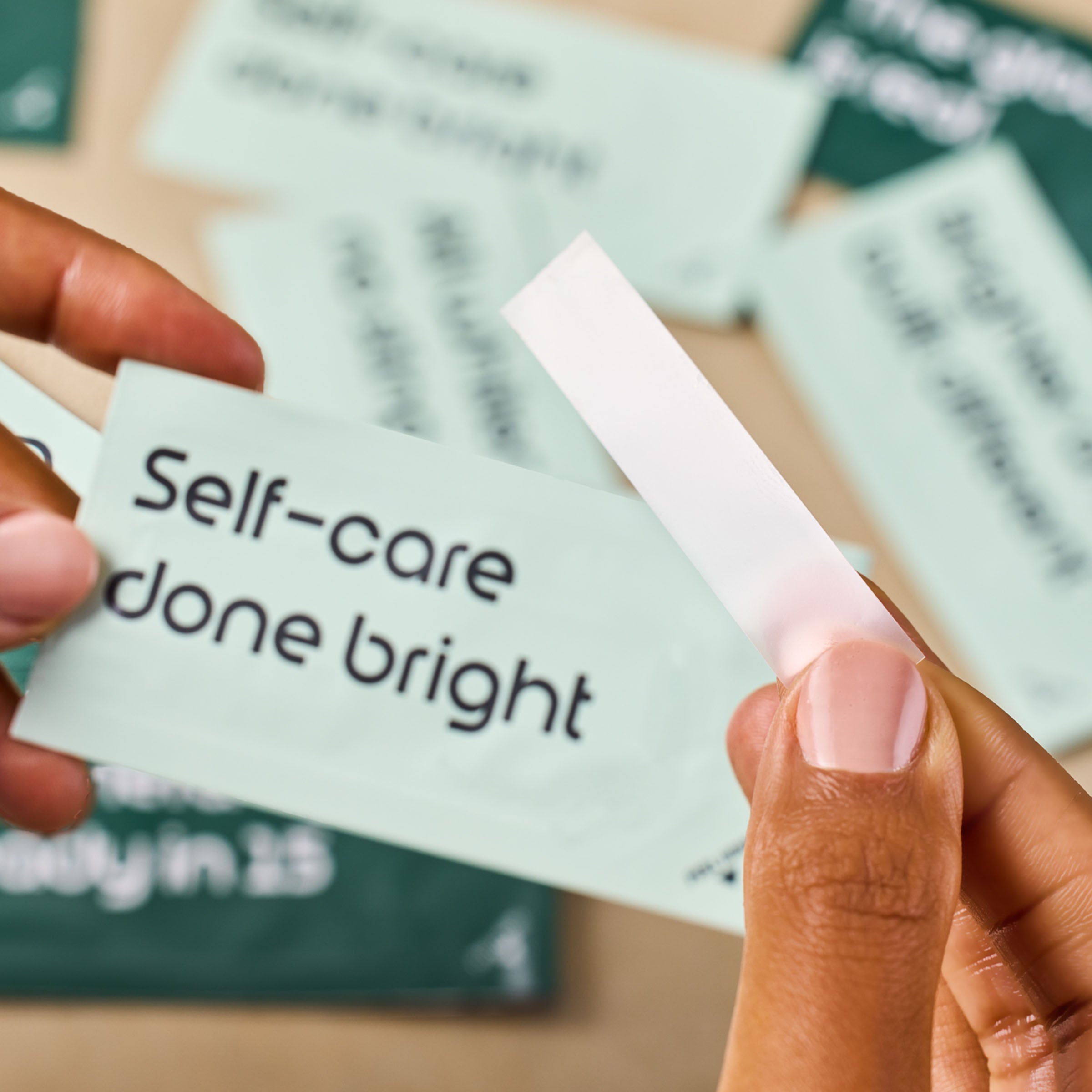 Hand holding a small card with 'Self-care done bright' text, with a blurred background of similar cards.