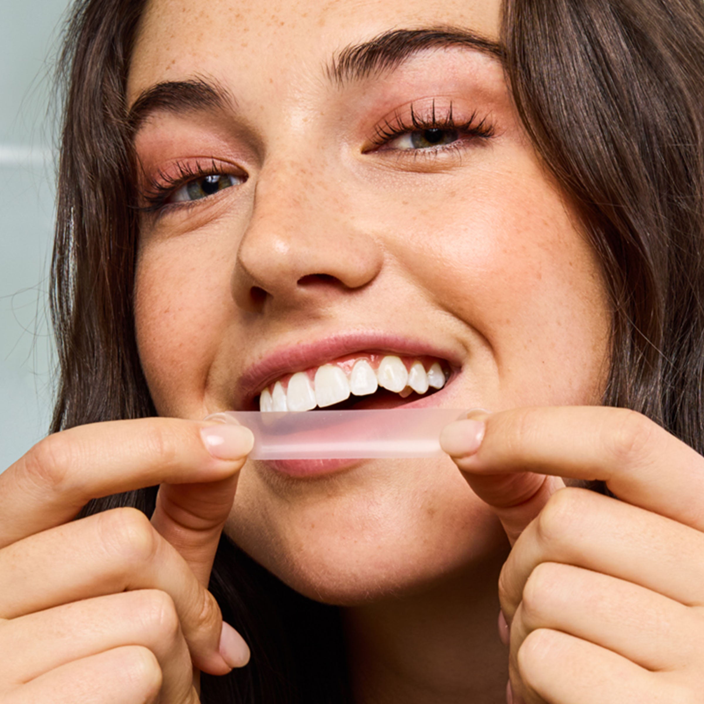 Woman holding a clear aligner between her fingers, showing a close-up of her face.