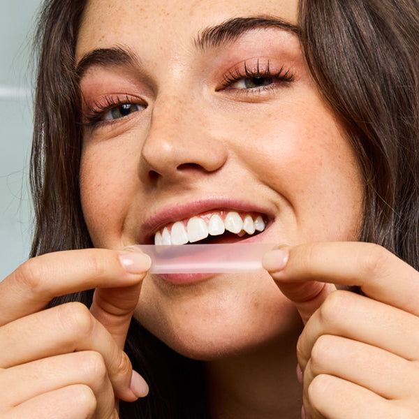 Woman holding a clear aligner between her fingers, showing a close-up of her face.