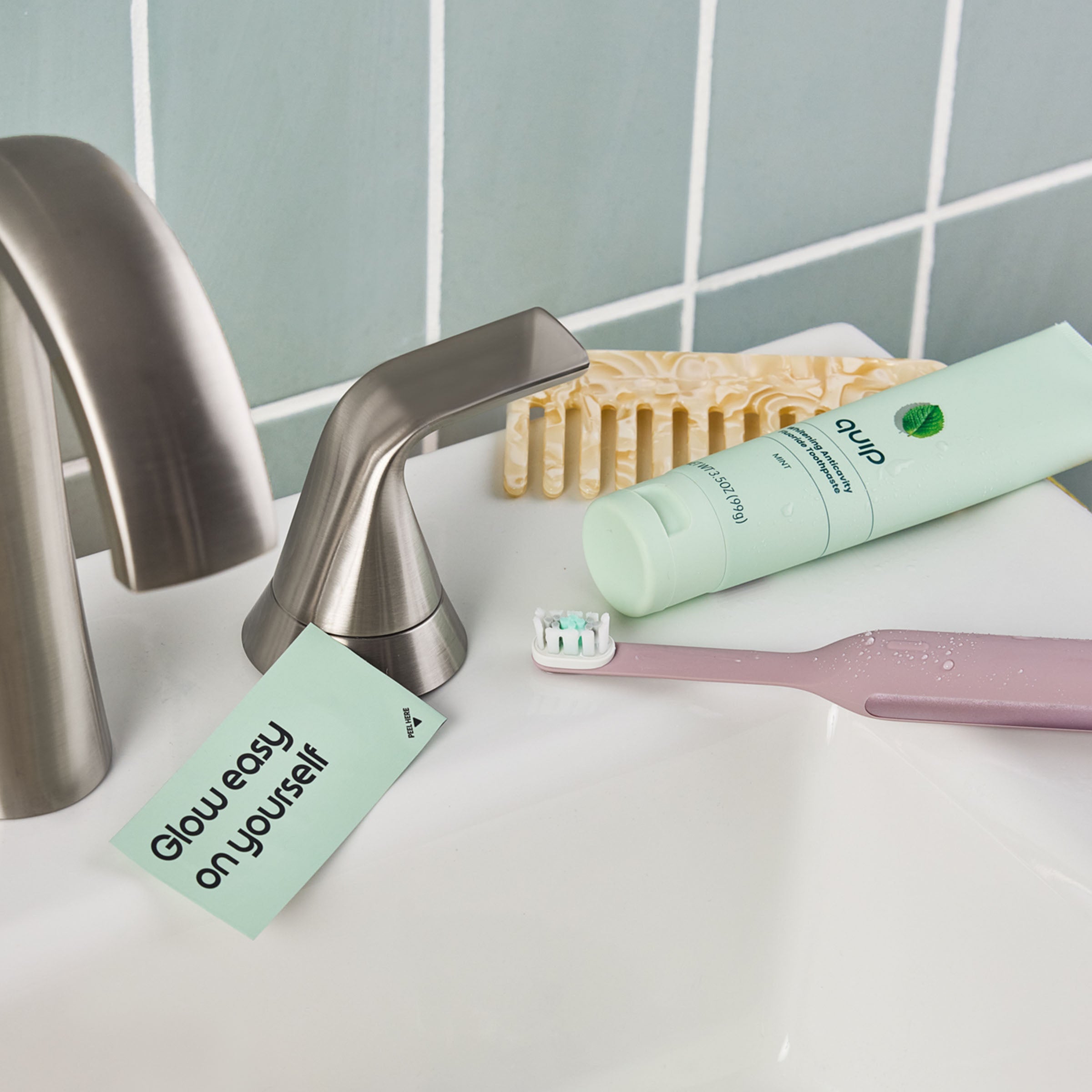 Toothbrush, toothpaste, and a card on a bathroom sink with a tiled wall background