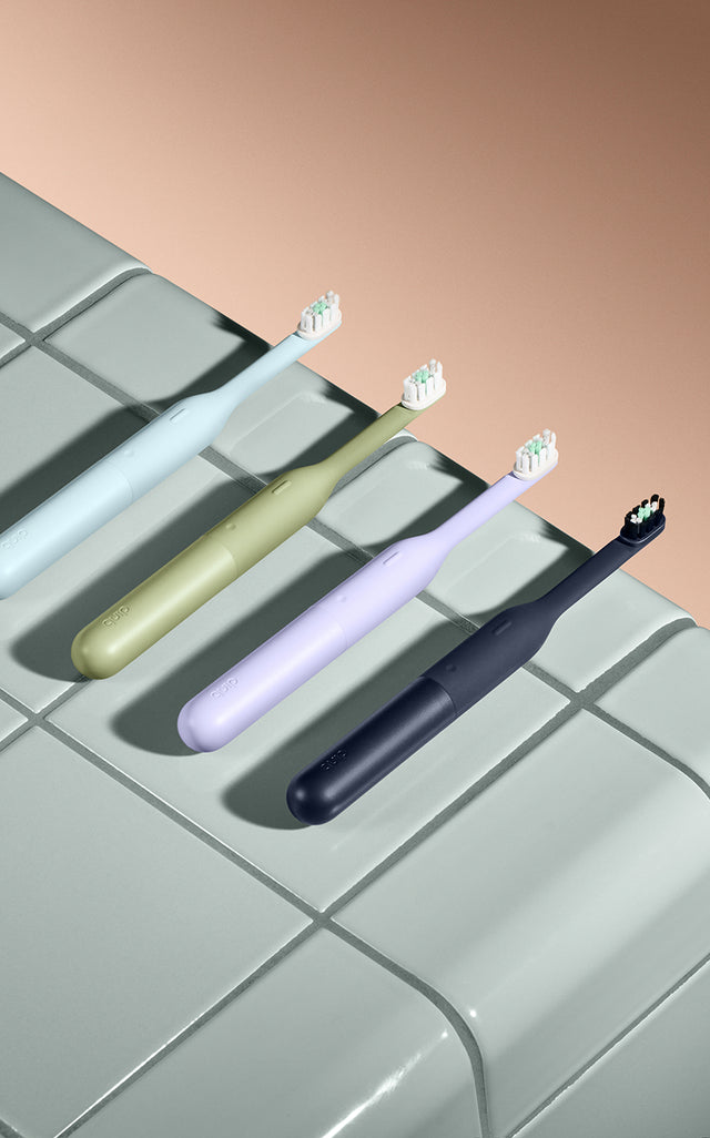 Four electric toothbrushes in different colors on a tiled surface.