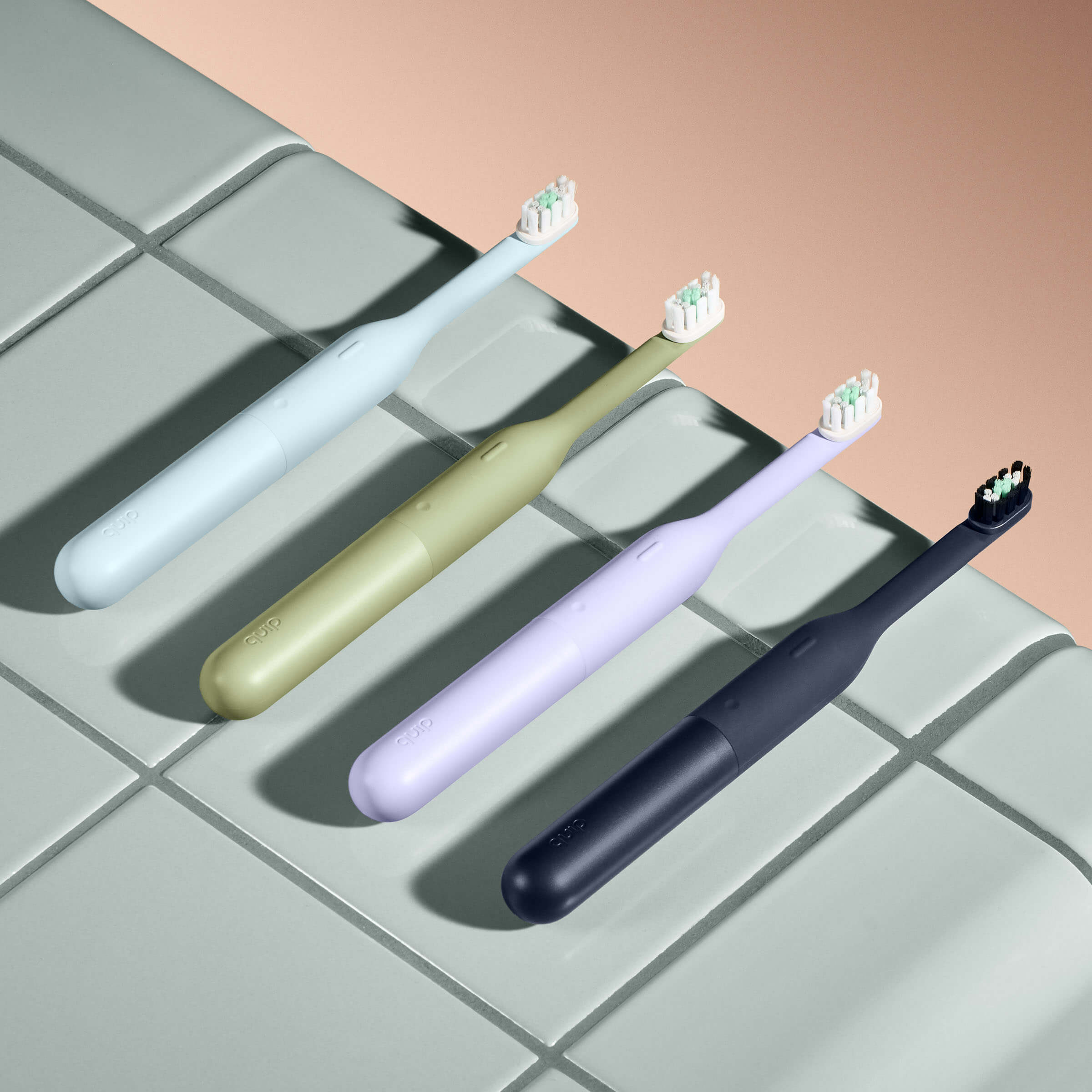 Four electric toothbrushes in different colors on a tiled surface.