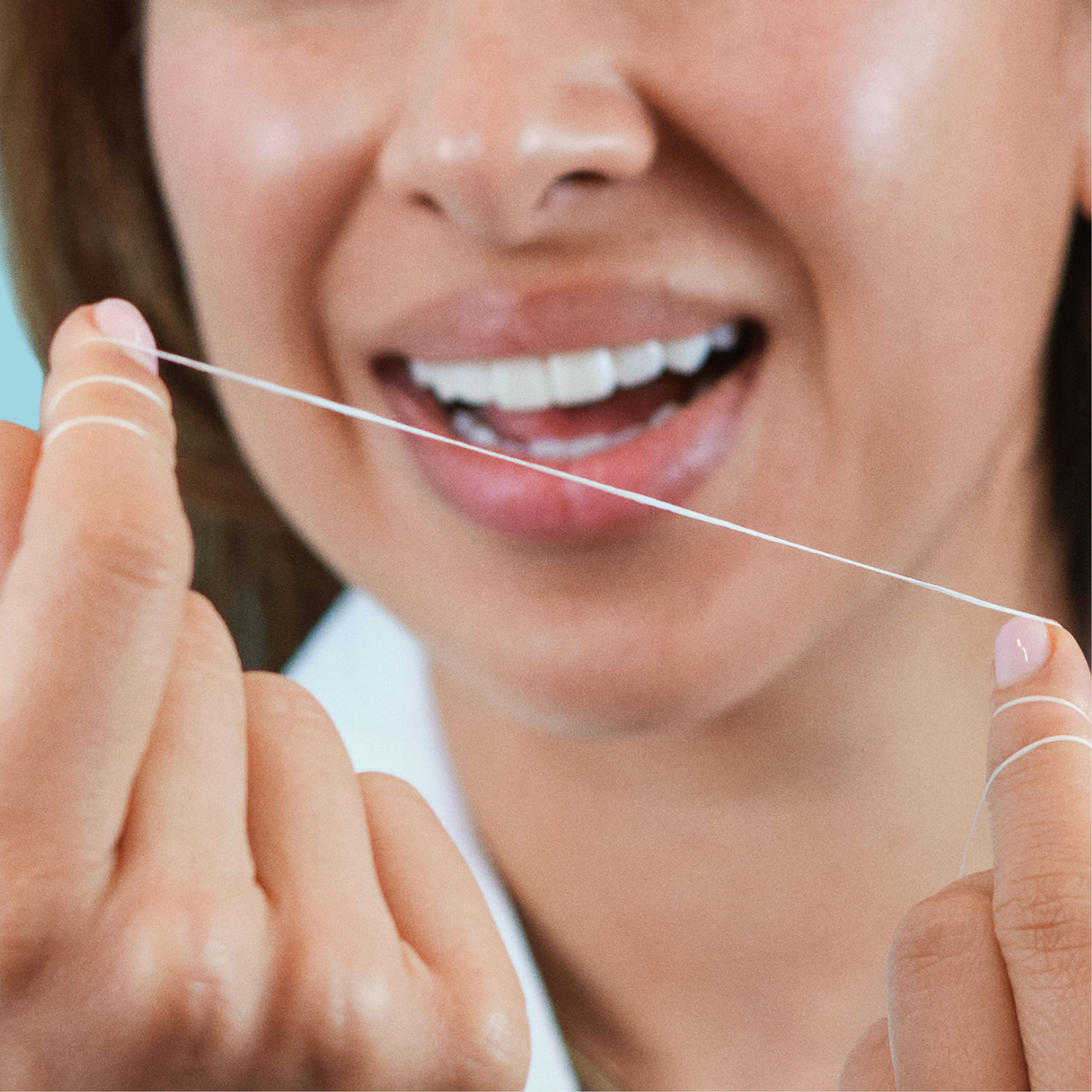 A close-up of a person holding dental floss between their fingers, demonstrating how to use it for oral hygiene.