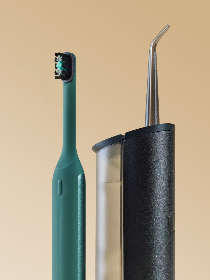 A teal oral irrigator toothbrush stands next to a black cylindrical water flosser canister with a curved metal nozzle, set against a solid beige background.